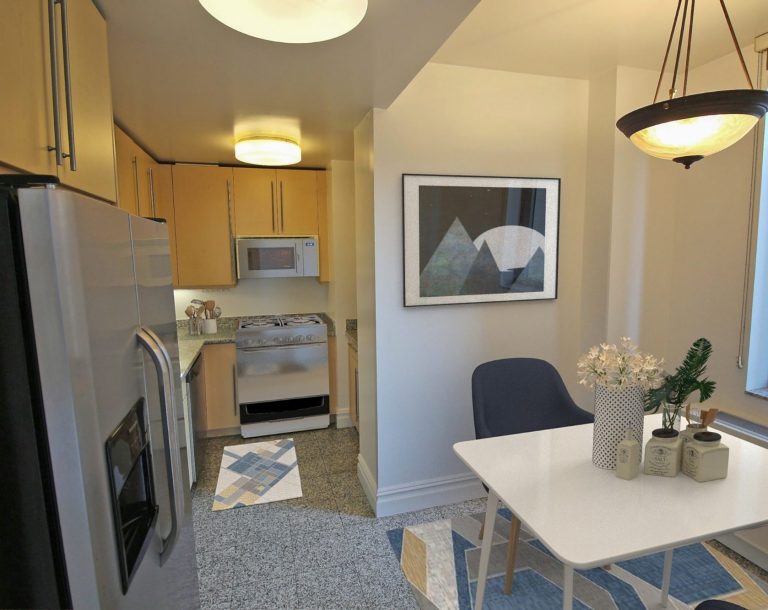 Photo of the eat-in-kitchen, showing a dinner table in the windwon, refrigerator, stove and many cabinets.