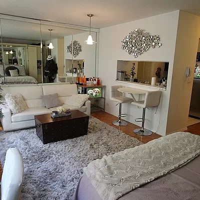 photo of the living room of the studio, showing the sofa, rug, center table, partial bed, and the window to the kitchen.